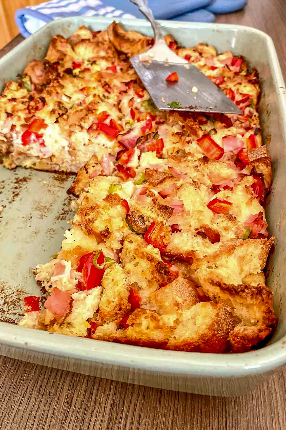Baking dish with Ham And Cheese Strata and a spatula for serving.