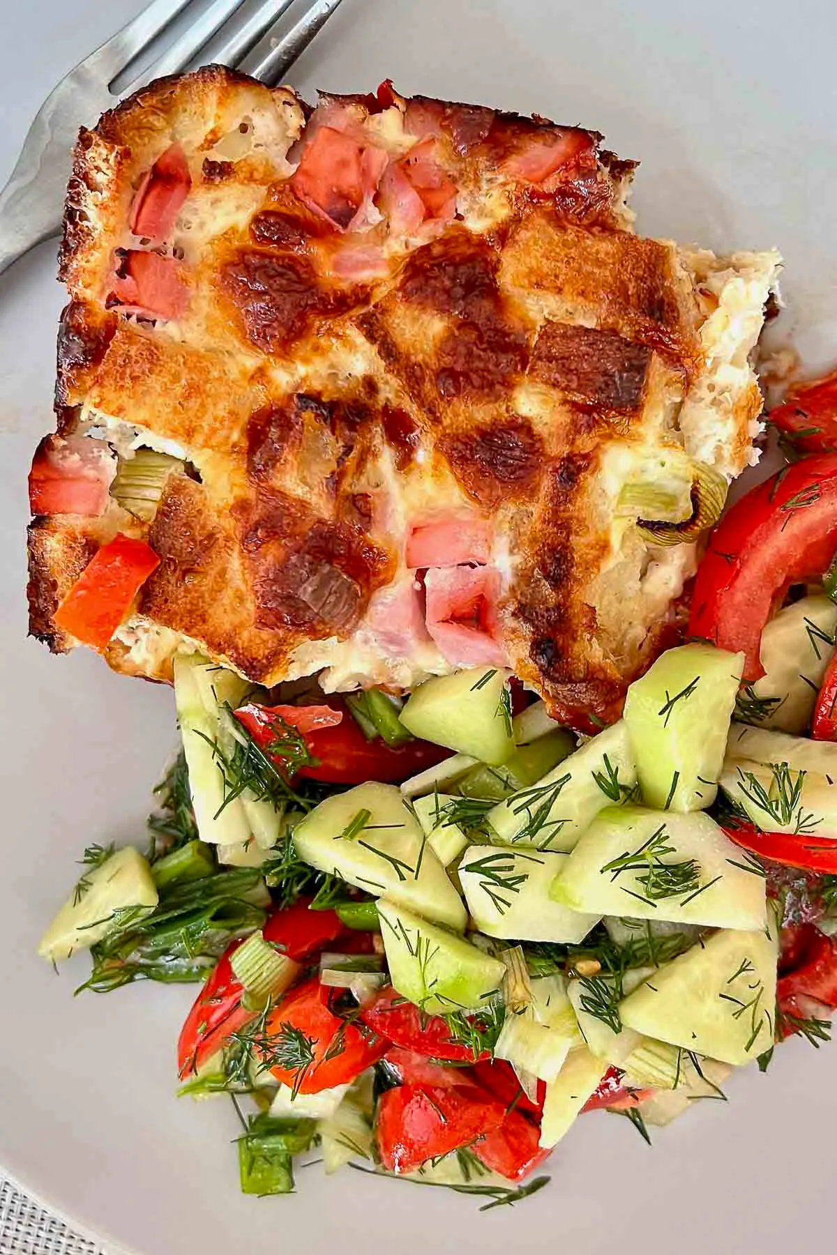 Ham And Cheese Strata Slice with tomato cucumber salad on white plate1200