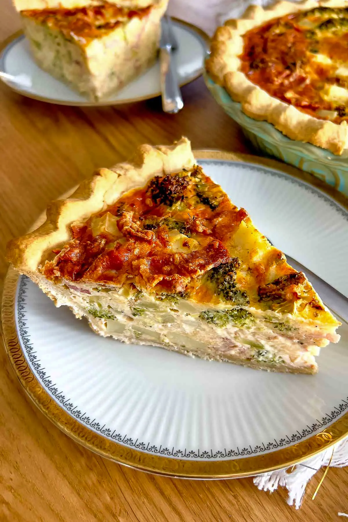 Slice of Broccoli Bacon Quiche on white plate with golden edge.