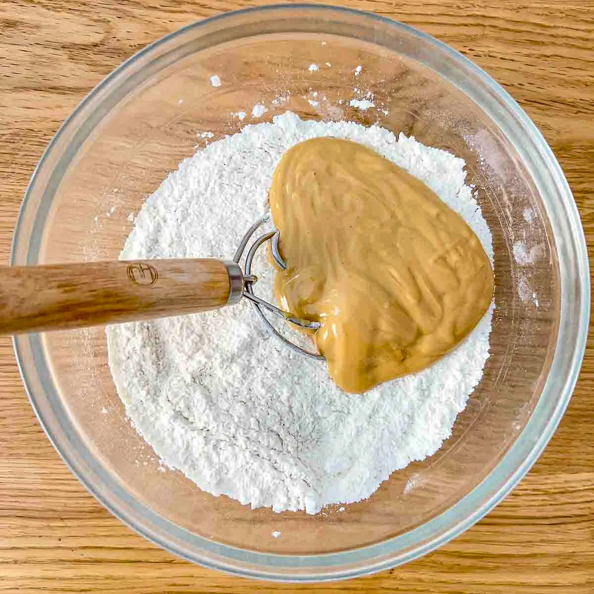 Mixing dry ingredients with peanut butter in a glass bowl.