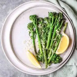 Roasted Broccolini With Garlic And Lemon on a white table served with slices of lemon.