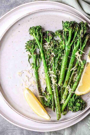 Roasted Broccolini With Garlic And Lemon on a white table served with slices of lemon.