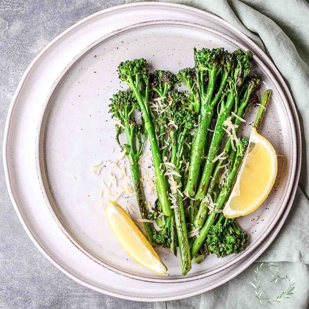 Roasted Broccolini With Garlic And Lemon on a white table served with slices of lemon.