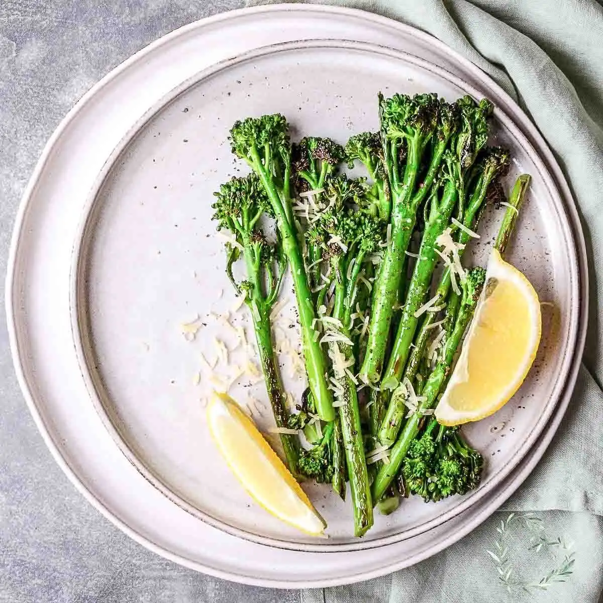 Roasted Broccolini With Garlic And Lemon on a white table served with slices of lemon.