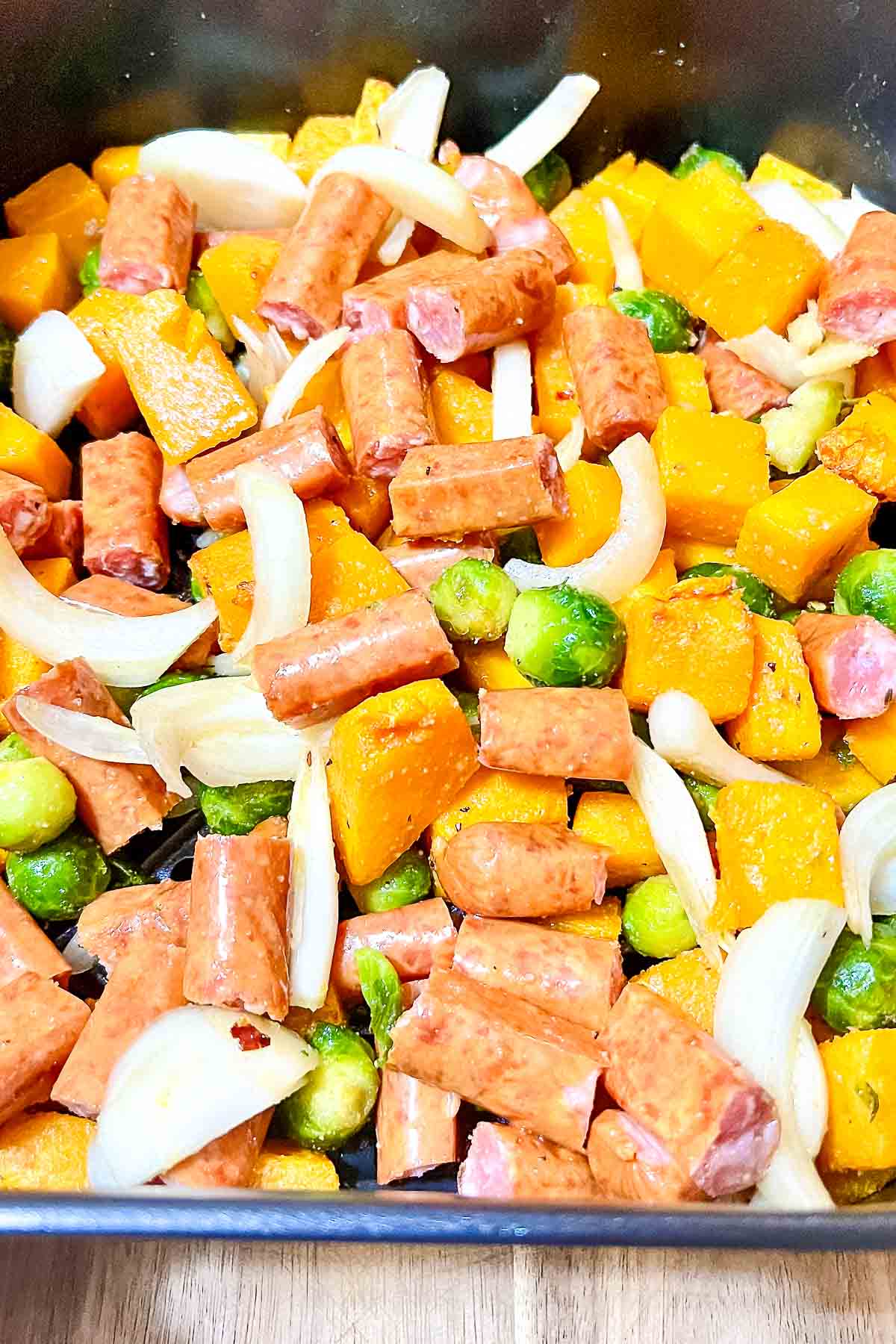 Adding onions and sausages to the vegetables.