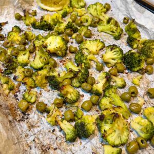Roasted broccoli and olives on a baking tray.
