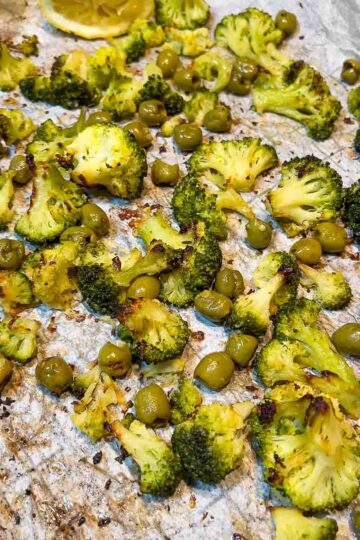 Roasted broccoli and olives on a baking tray.