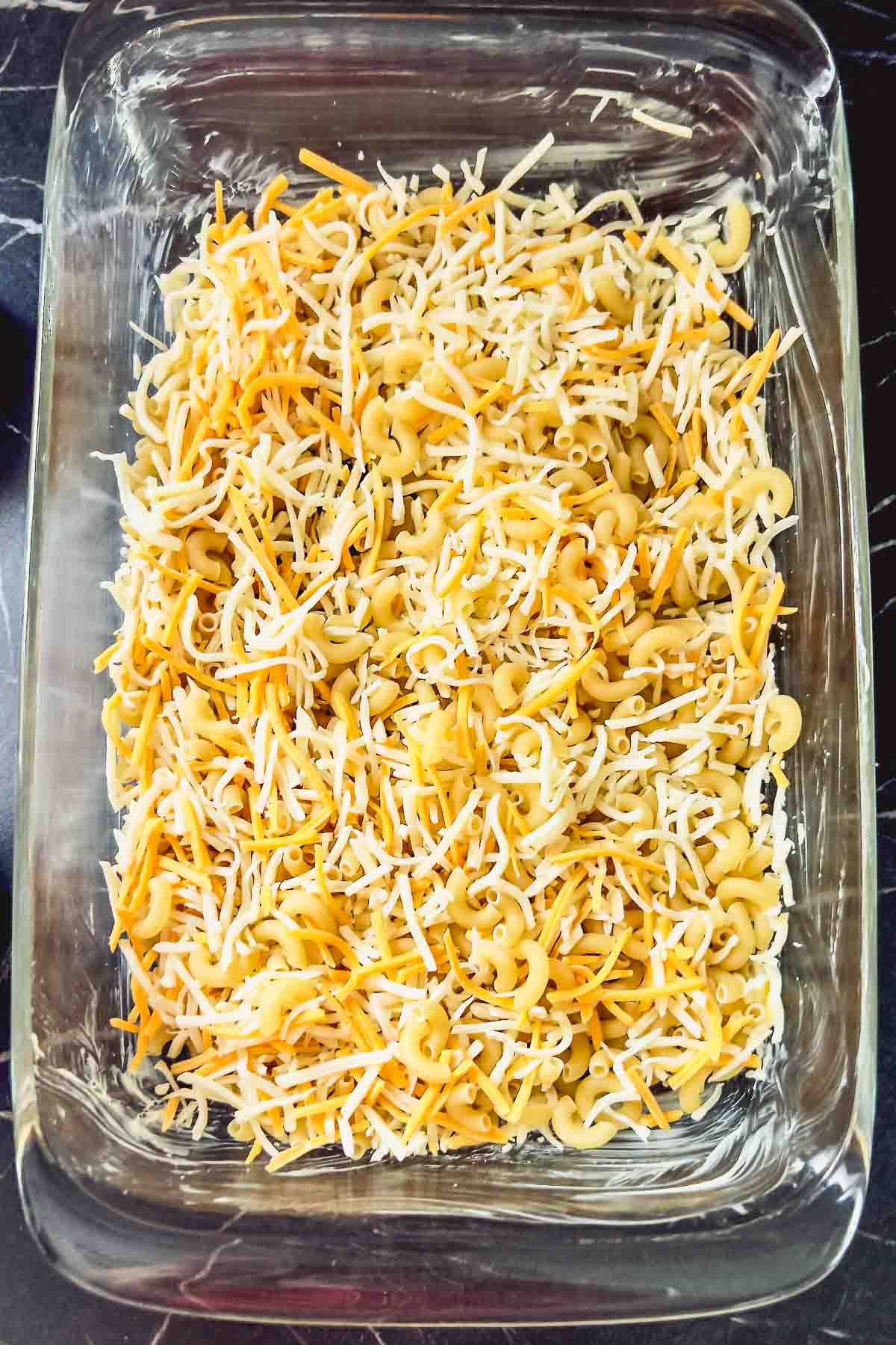 Uncooked pasta with shredded cheese in a 9x13inch pan.